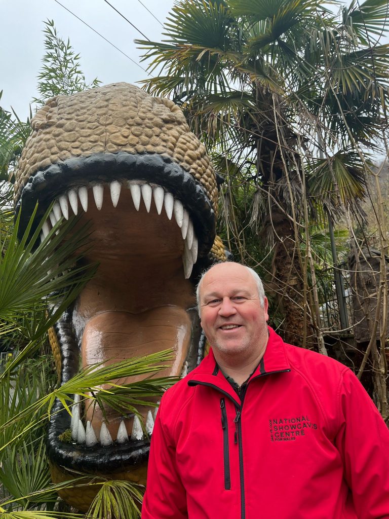 Carl Shaw standing in front of a large dinosaur model at the National Showcaves Centre for Wales