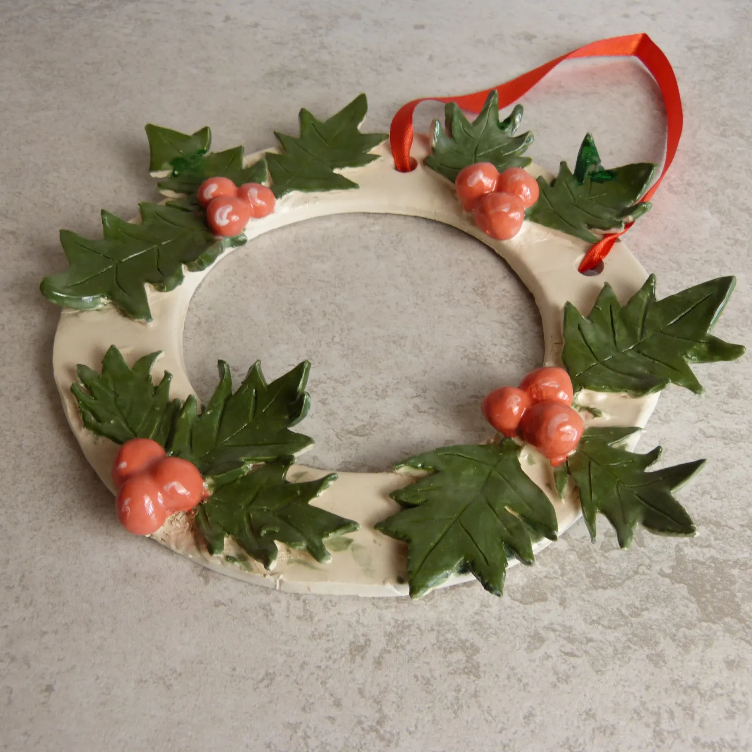Handmade ceramic Christmas wreath decorated with green leaves and red berries