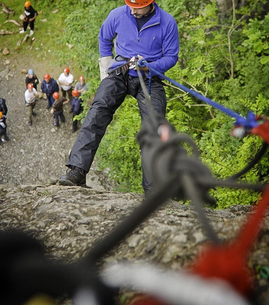 Instructor demonstrating an abseil on a rock face with a group waiting below