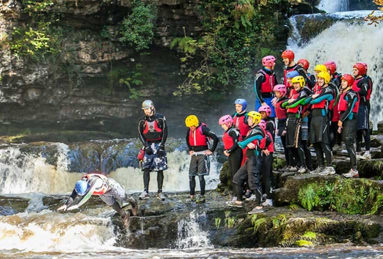 Group wearing helmets and buoyancy aids beside a waterfall during an Adventure Britain gorge walk