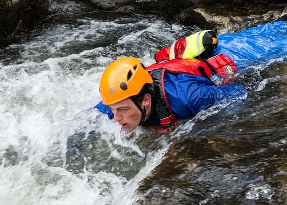 Participant in a helmet and buoyancy aid moving through fast-flowing water on an Adventure Britain gorge session