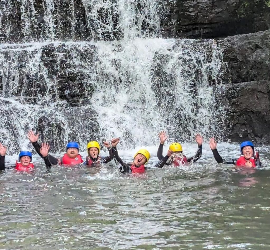 Group of participants in helmets and buoyancy aids celebrating in a waterfall pool