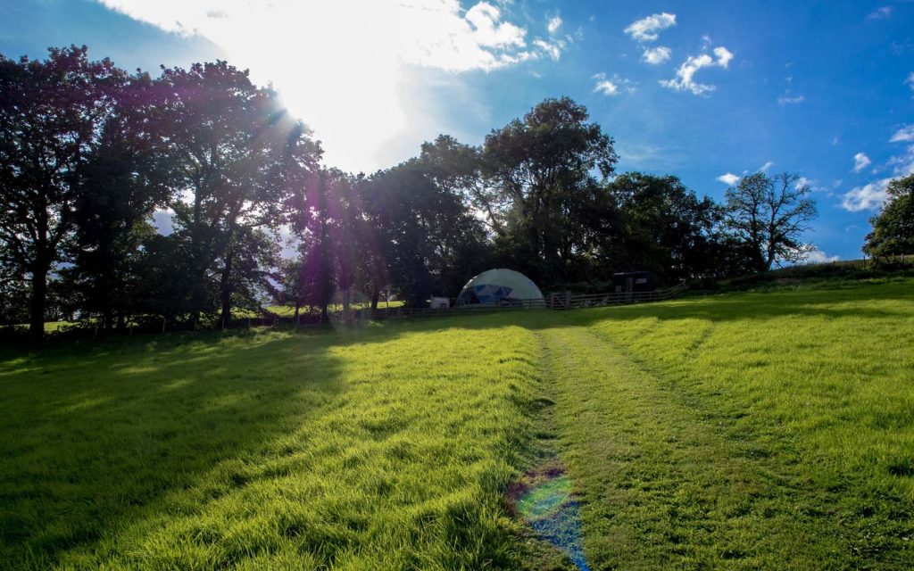 Glamping dome in a green hillside field beneath blue sky at Argoed Barns