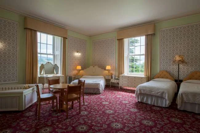 Bright en-suite bedroom with twin beds and large windows at Baskerville Hall Hotel