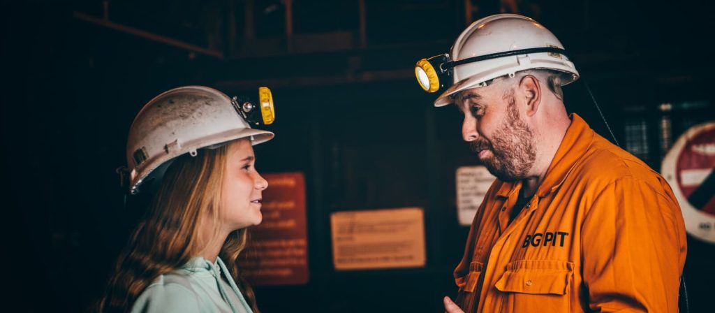 Former miner in an orange Big Pit uniform speaking to a visitor