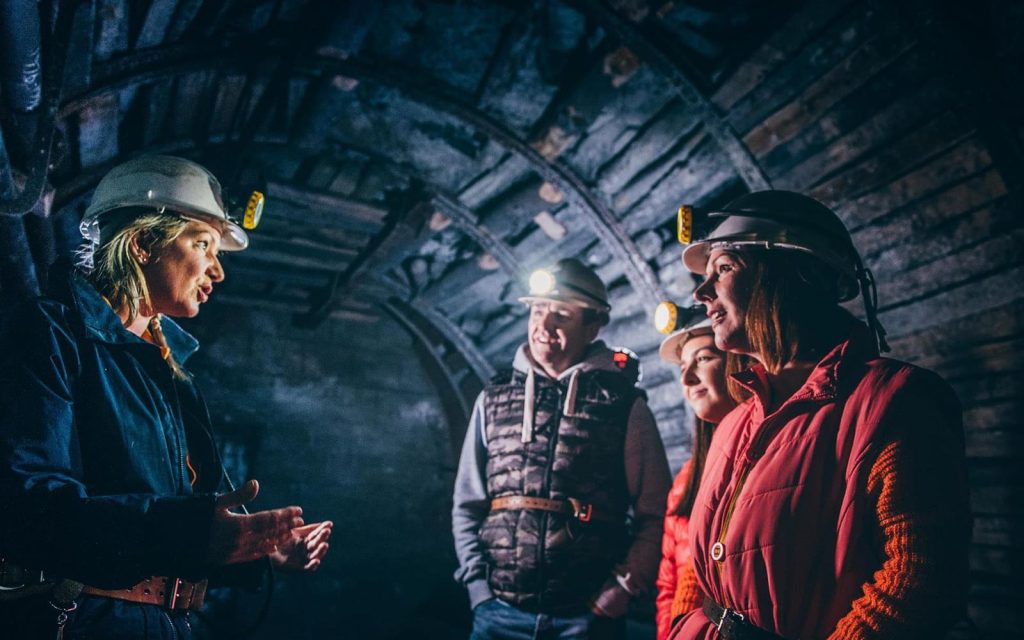 Visitors wearing miners’ helmets listening to a guide underground at Big Pit