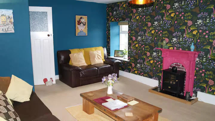 Blue and floral living area with a stove and sofas inside the Camp Cynrig cabin