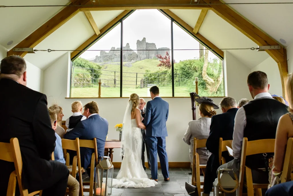 Wedding ceremony inside a light-filled Carreg Cennen venue with the castle visible beyond