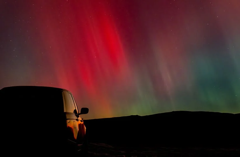 Red and green aurora glowing above a dark Welsh hillside