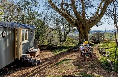 Shepherd hut beneath trees with outdoor seating from Dog Friendly Cottages