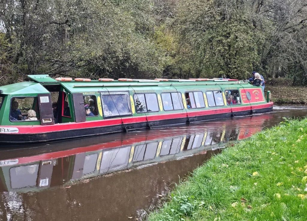 Dragonfly passenger boat reflected in the wooded Monmouthshire and Brecon Canal