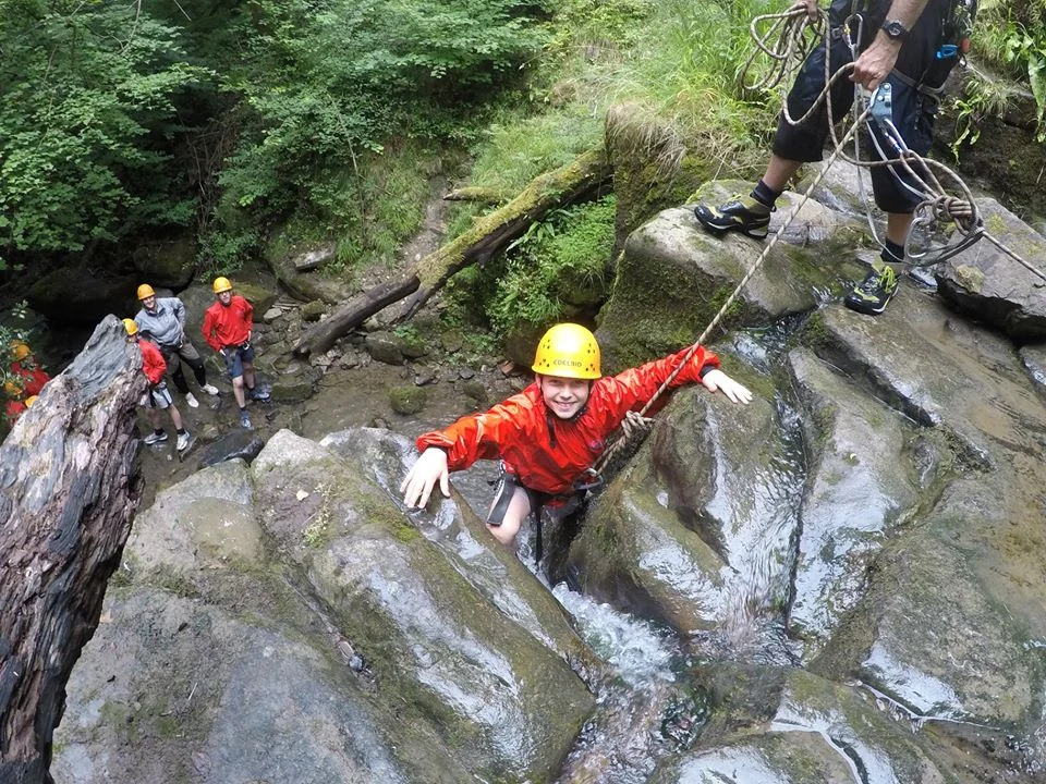 Group scrambling over rocks in a wooded gorge with Inspire2Adventure