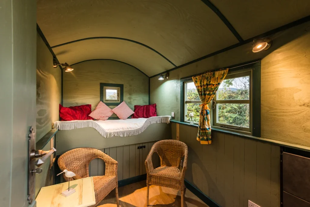 Double bed and two wicker chairs inside a curved-roof shepherds hut