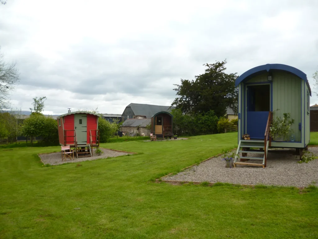 Three colourful shepherds huts spaced across a grassy site near Llangorse
