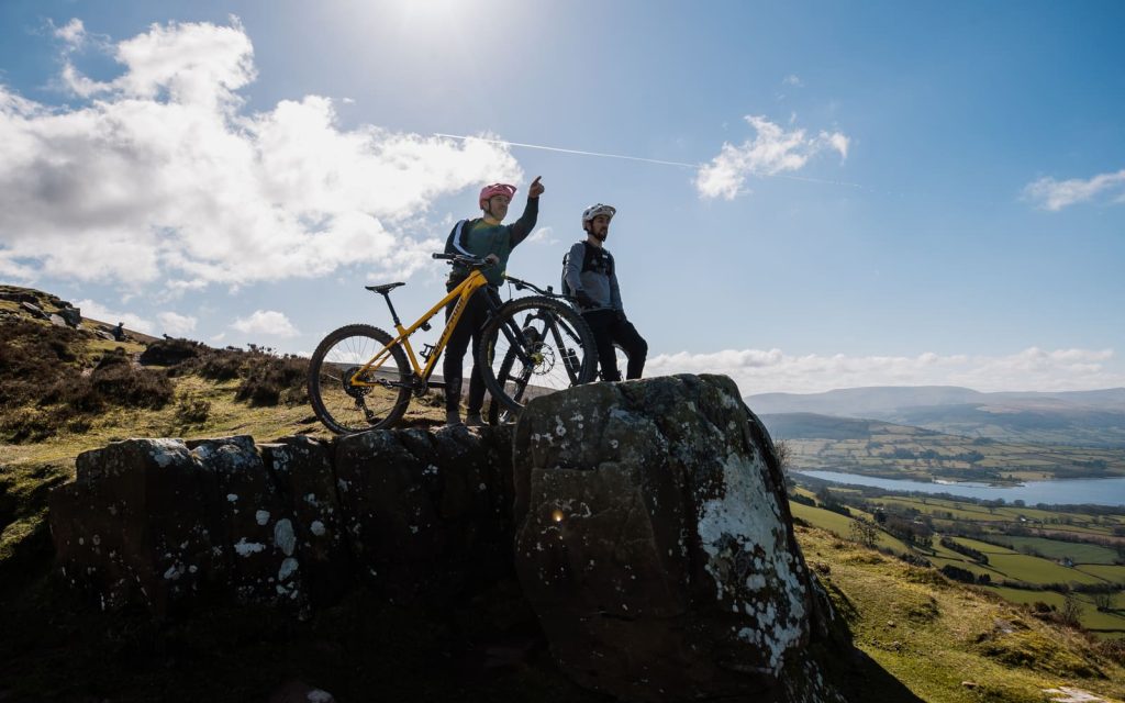 Two riders with mountain bikes on a rocky viewpoint above the valley